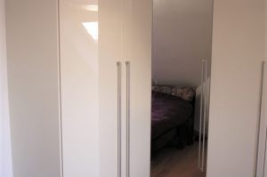 Schlafzimmer- Einbauschrank in Senosan Creme Brilliantglanz mit Edelstahl- Relinggriffen (als komplette Raumlösung an drei Zimmerwänden)