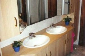 Badezimmermöbel mit 3D-Spiegelschrank- Überbau in Rundkantenfronten HPL Apfel. Waschtisch und Kranzplatte in HPL Apfel belegt