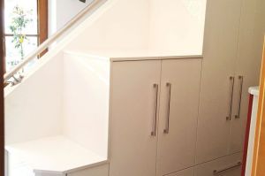 Stufige Schrankanlage in weiß Hochglanz vor der Treppenwand als Schuh und Garderobeschrank
